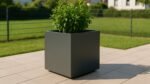 Anthrazitfarbener quadratischer Pflanzkübel aus Aluminium IVO Mobile auf einer Gartenterrasse, bepflanzt mit einem dichten grünen Strauch