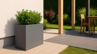 A Pflanzkübel aus Aluminium Rechteckig 90cm x 30cm x H 80cm EDOARDO 1 in Grau, bepflanzt mit grünen Sträuchern, steht auf hellem Holzboden vor einer weißen Wand, nahe einer Terrasse mit Pergola und Essgruppe im Garten.