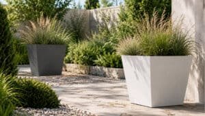 Zwei trapezförmige Aluminium-Pflanzkübel in Weiß und Grau mit unterschiedlichen Ziergräsern in einem sonnigen Garten