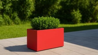 Der rechteckige Pflanzkübel aus Aluminium EDOARDO 8 (100x50xH50cm, jede RAL Farbe) steht bepflanzt auf einer hellgrau gefliesten Terrasse, dahinter ein dichter grüner Rasen - perfekte Gartenidylle im Sonnenlicht.