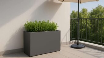 Auf einem modernen Balkon mit hellgrauen Fliesen steht ein Pflanzkübel aus Aluminium Rechteckig 120cm x 40cm x H 80cm EDOARDO 19 jede RAL Farbe gefüllt mit Grünpflanzen. Ein schwarzes Metallgeländer und ein beiger Regenschirm auf einem runden Ständer spenden Schatten, im Hintergrund stehen Bäume.