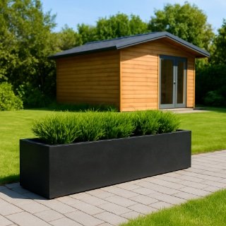 Ein moderner schwarzer rechteckiger großer Blumentopf mit grünen Sträuchern steht auf einem gepflasterten Weg der Terrasse, vor einem kleinen hölzernen Gartenschuppen mit Glastüren, umgeben von Bäumen im Hintergrund.