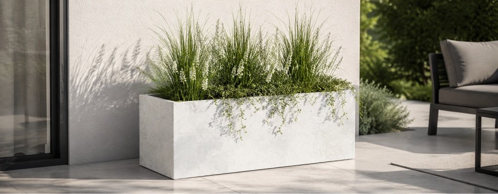 Rechteckiger Pflanzkübel in Betonoptik mit Ziergräsern und weißen Blüten auf einer modernen Terrasse