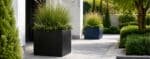 Moderne Fiberglas-Pflanzkübel in Schwarz und Blau mit grüner Bepflanzung auf einem hellen Gartenweg