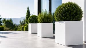 Weiße Pflanzkübel in RAL 9016 mit grünen Pflanzen auf einer modernen Terrasse im Außenbereich.