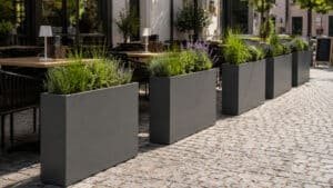 Anthrazitfarbene rechteckige Aluminium-Pflanzgefäße mit Ziergräsern und blühenden Stauden als elegante Abtrennung eines Restaurant-Außenbereichs.