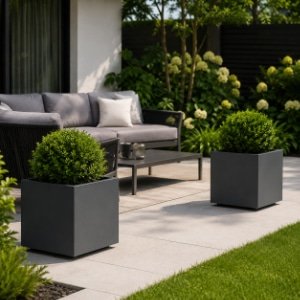 Aluminium-Pflanzkübel mit kugelförmig geschnittenen grünen Pflanzen neben modernen Gartenmöbeln auf einer Terrasse