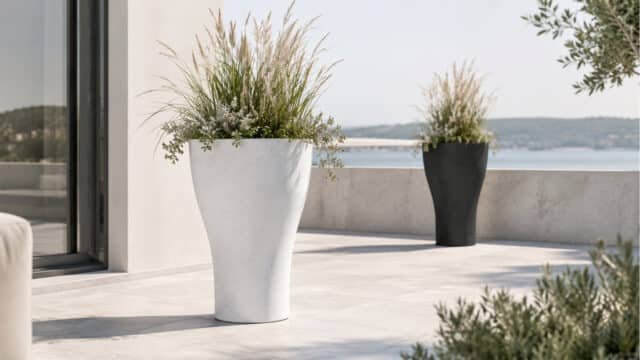 Beton-Pflanzkübel in Weiß und Schwarz mit dekorativen Gräsern auf einer hellen modernen Terrasse, einer im Vordergrund und einer im Hintergrund