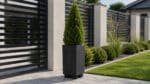 Betonpflanzkübel mit einer grünen Thuja vor einem modernen Gartenzaun auf gepflastertem Boden