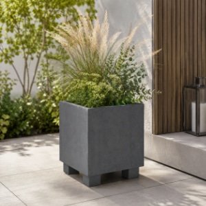 Quadratischer grauer Beton-Pflanzkübel mit Ziergräsern und grünen Pflanzen auf einer modernen Terrasse