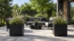 Pflanzkübel mit Ziergräsern und Wildblumen neben einer modernen Outdoor-Lounge auf der Terrasse