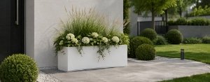 Pflanzkübel mit Ziergräsern, weißen Blüten und hängenden Grünpflanzen vor einem modernen Hauseingang