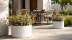 Pflanzkübel mit bunten Wildblumen stehen auf einer modernen Terrasse neben Tisch und Stühlen
