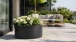 Pflanzkübel mit weißen Blumen auf einer modernen Terrasse, im Hintergrund stehen stilvolle Gartenmöbel