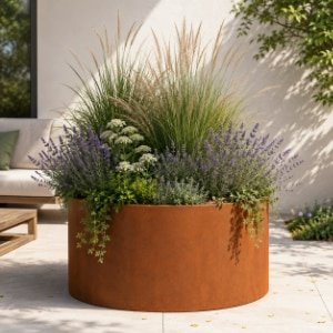 Großes rundes Cortenstahl-Pflanzgefäß mit Lavendel, weißen Blüten, Ziergräsern und grünen Pflanzen auf einer hellen Terrasse