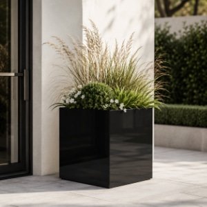 Hoher schwarzer Fiberglas-Pflanzkübel mit Ziergräsern, grünen Pflanzen und weißen Blüten vor einem modernen Hauseingang